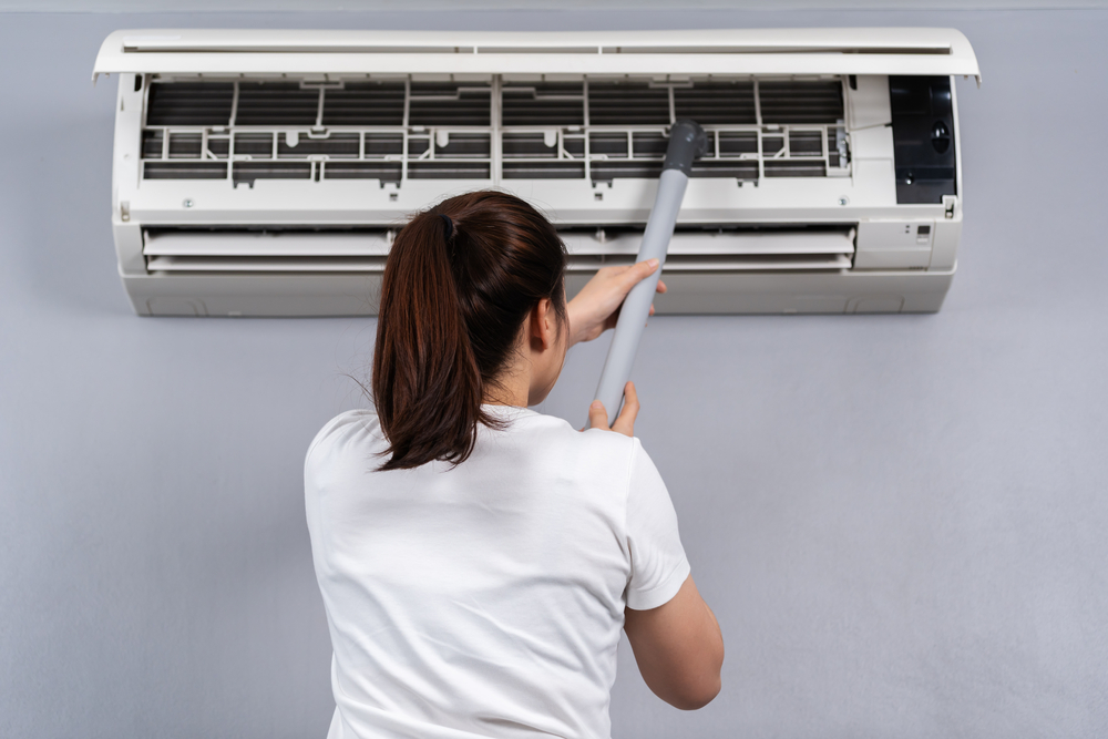 Young woman using vacuum cleaner to cleaning the air conditioner at home.